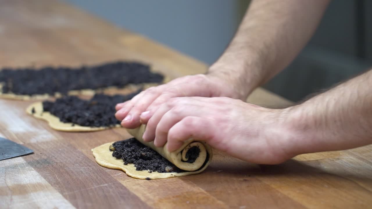 manos rodando cuidadosamente la masa llena de semillas de amapola para preparar el tradicional bejgli de navidad húngaro