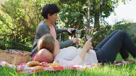 caucasian lesbian couple drinking wine together in the garden during picnic