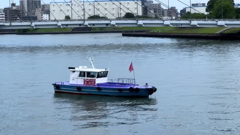 a small boat with a red flag floats on a calm river near an urban area