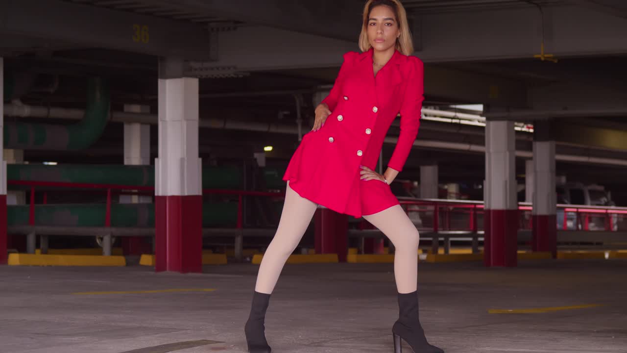 Nel cuore della vita cittadina, una giovane ragazza di origine ispanica si aggira in un parcheggio multipiano, vestita con un corto abito rosso.