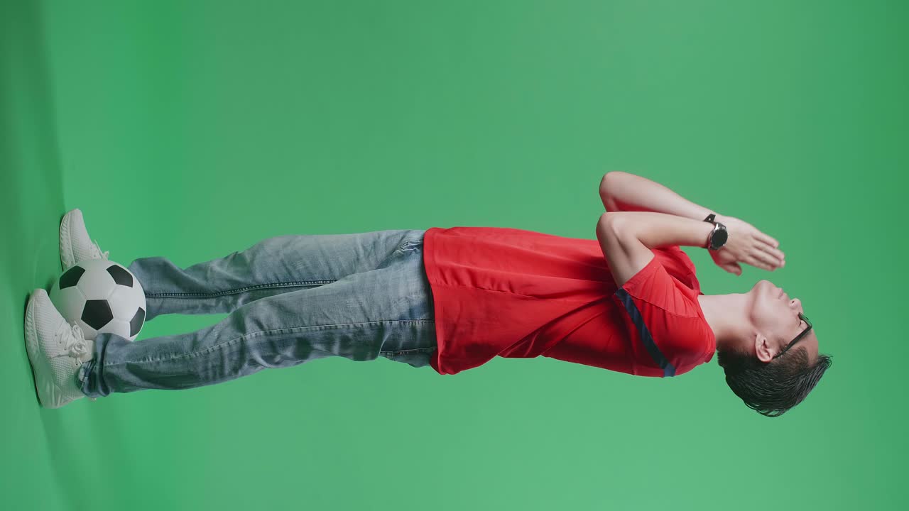 cuerpo lleno de ojos cerrados hombre asiático con una pelota rezar por un equipo antes de levantar la mano mientras aplaude el fútbol en el fondo de la pantalla verde