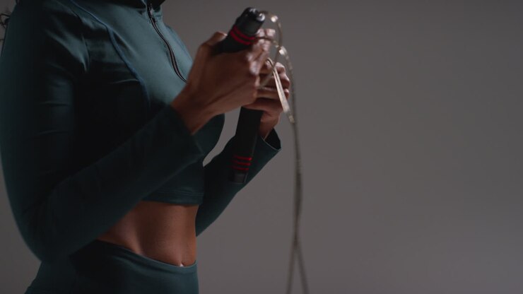 Close Up Shot Of Female Athlete Wearing Tracksuit Training In Gym Fitness Class With Jump Rope Or Skipping Rope Against Plain Background 2