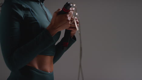 close up shot of female athlete wearing tracksuit training in gym fitness class with jump rope or skipping rope against plain background 2