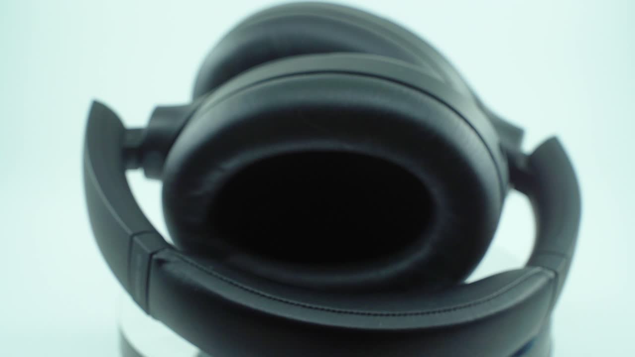 un primer plano cinematográfico, video de producto 4k, auriculares inalámbricos negros, auriculares suaves, luz de estudio, cámara lenta, soporte reflectante giratorio