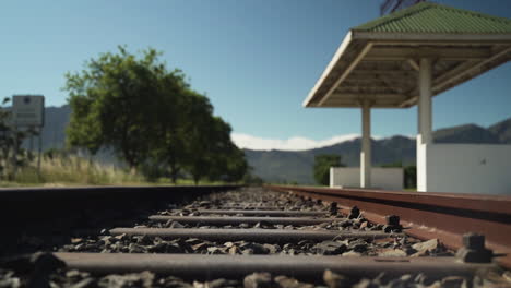 an old abandoned railway station with empty railway tracks and a background of trees and mountains with blue sky