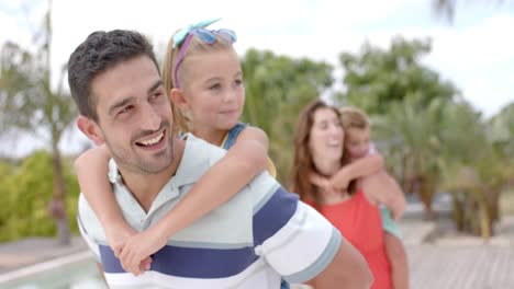 Happy-caucasian-parents-carrying-children-at-swimming-pool-at-beach-house