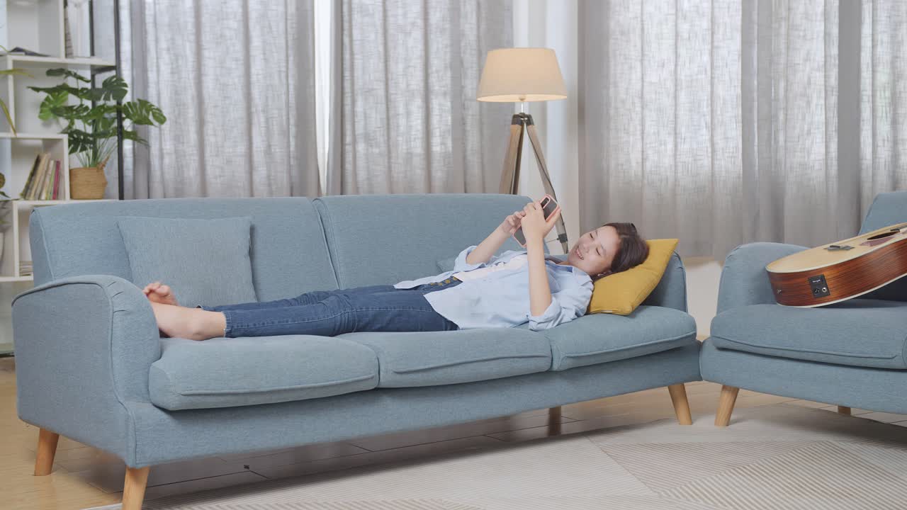 여자 는 전화 를 들고 소파 에서 휴식 을 하고 있다