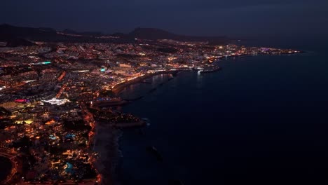 destino de vacaciones popular de costa adeje en la isla de tenerife, islas canarias, vista aérea nocturna siguiendo de derecha a izquierda.