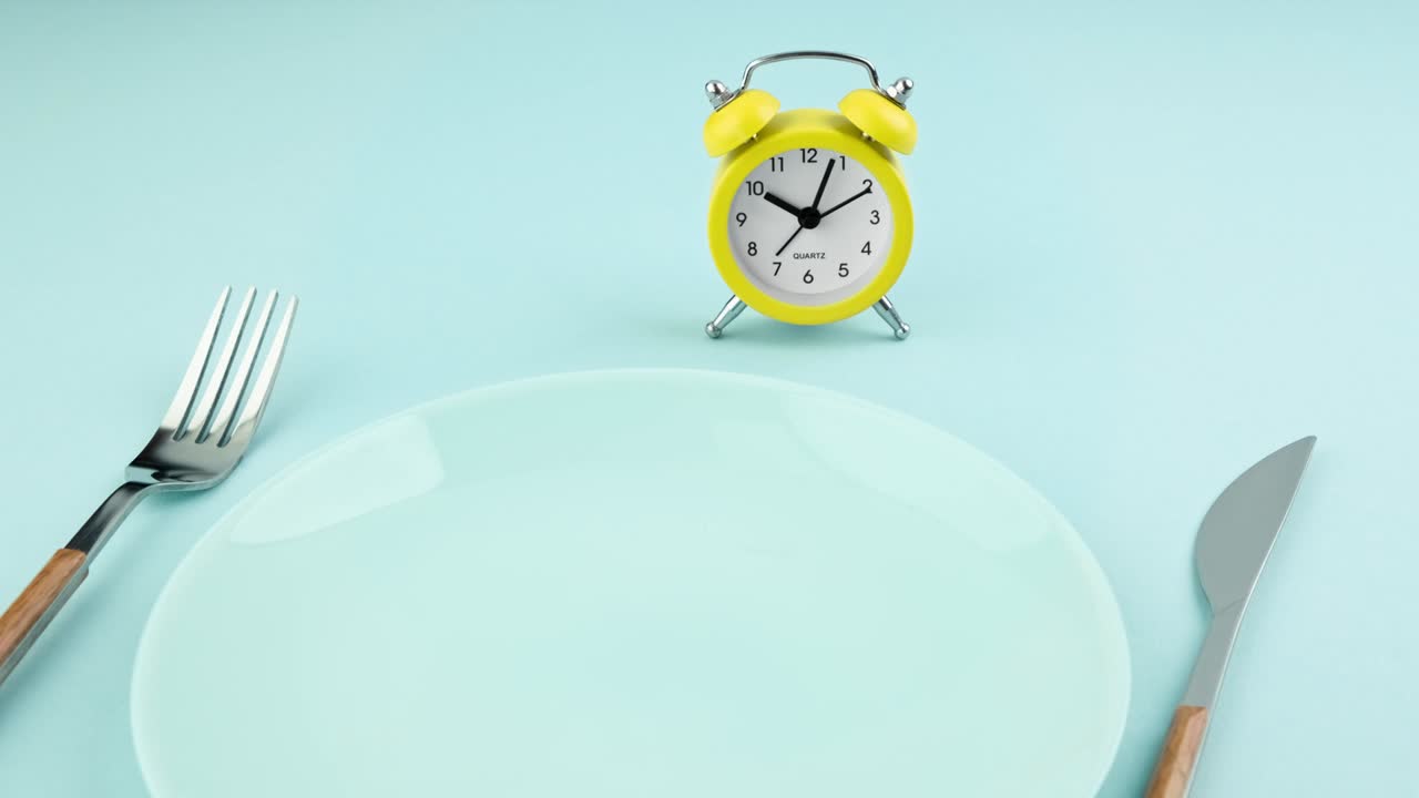 ayuno intermitente, dieta, concepto de la hora del almuerzo. despertador amarillo, plato vacío y cubiertos.