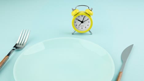 intermittent fasting, diet, lunch time concept. yellow alarm clock, empty plate and cutlery.