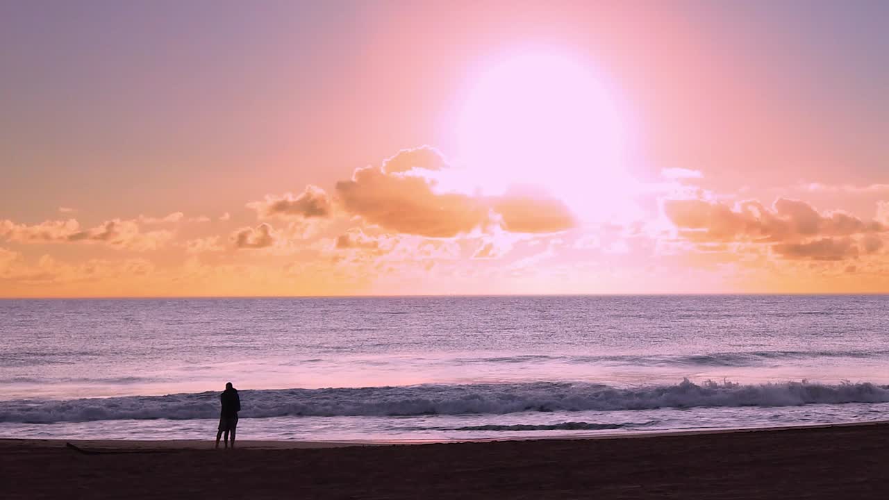 HD Hawaii Kauai HYBRID motionlapse timelapse zoom in of couple in distance on beach watching sunrise. Sunrise is timelapse, couple watching and ocean waves in normal speed.  Nice effect!