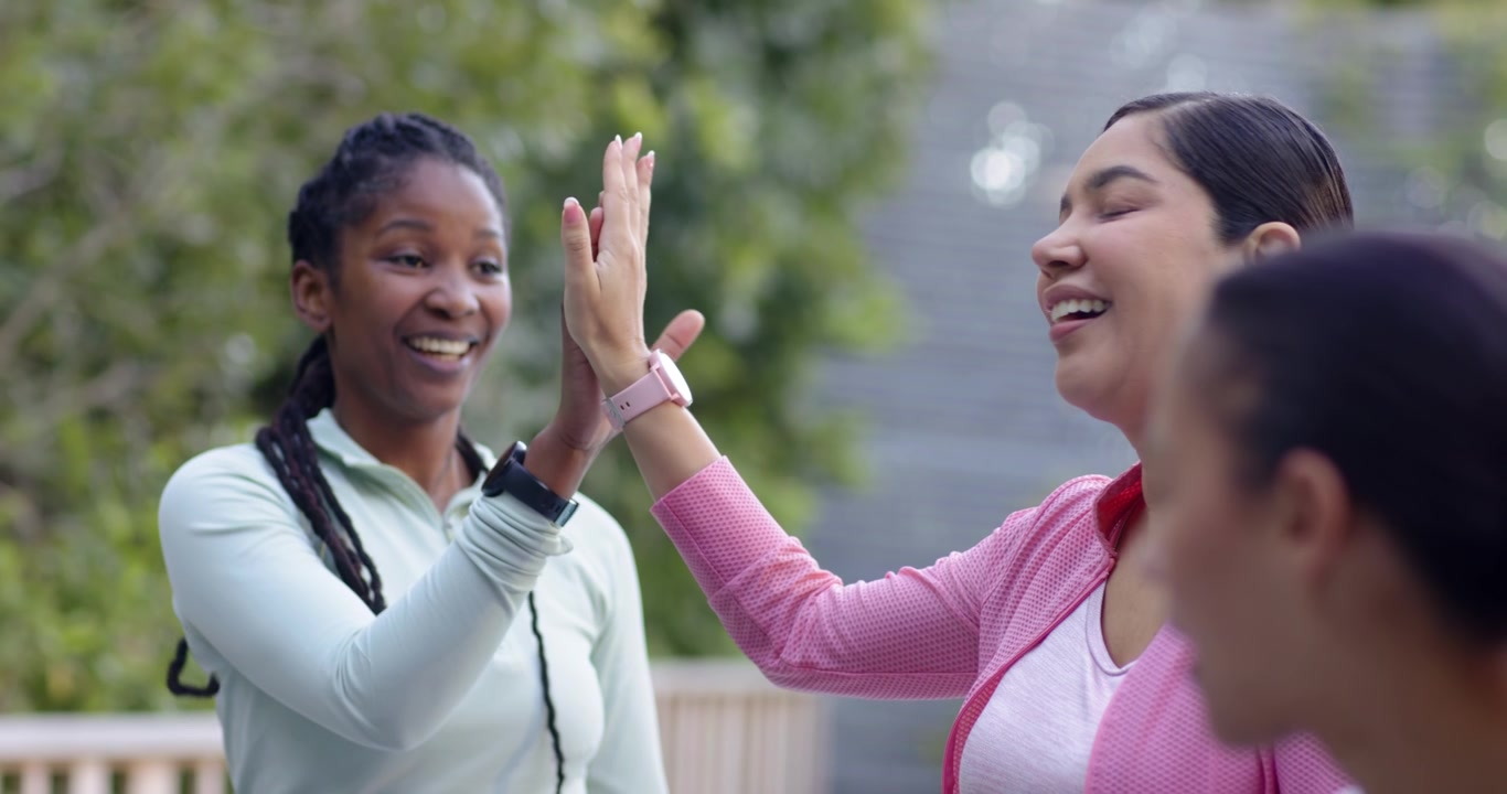 Diverse female friends greeting with high fives as pink jacket raising hand on deck with trackers