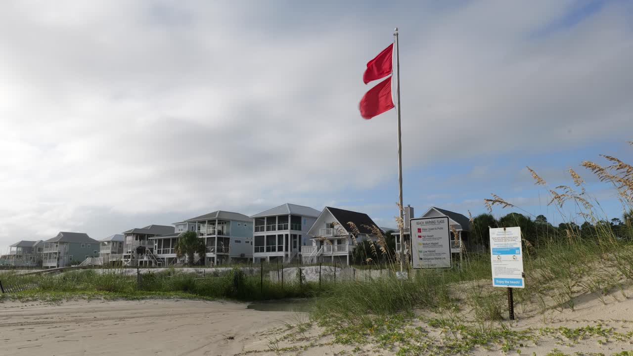 Double red flags indicating closed waters next to a beach access road and informational signs on Cape San Blas in the Florida panhandle.