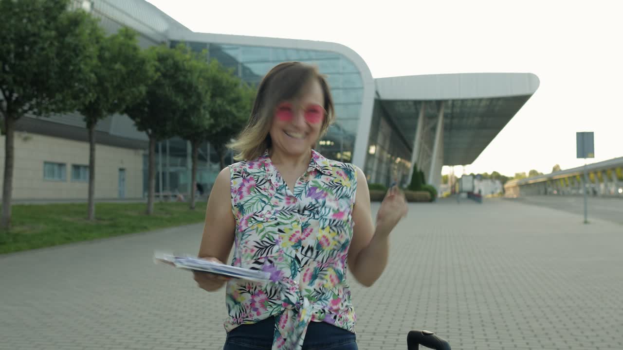 mujer turista caminando con equipaje desde el aeropuerto. la chica se detiene y comienza a sonreír, se regocija. vacaciones