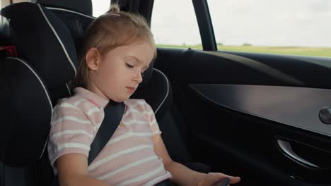 niña caucásica de 6 años usando teléfono móvil mientras viaja en coche.