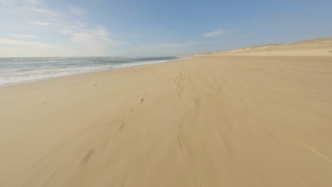 Aerial-fpv-racing-drone-flying-over-sandy-beach-and-sea-waters,-Landes-department-in-France