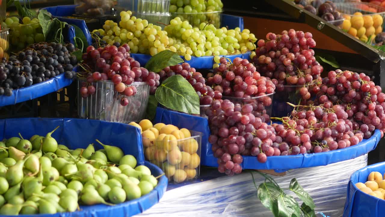 primer plano de un puesto de frutas con uvas, albaricoques y peras