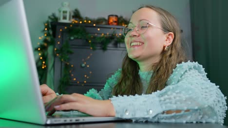 joven comprando regalos de navidad en línea escribiendo y sonriendo usando una computadora portátil con decoraciones de navidad de fondo en casa