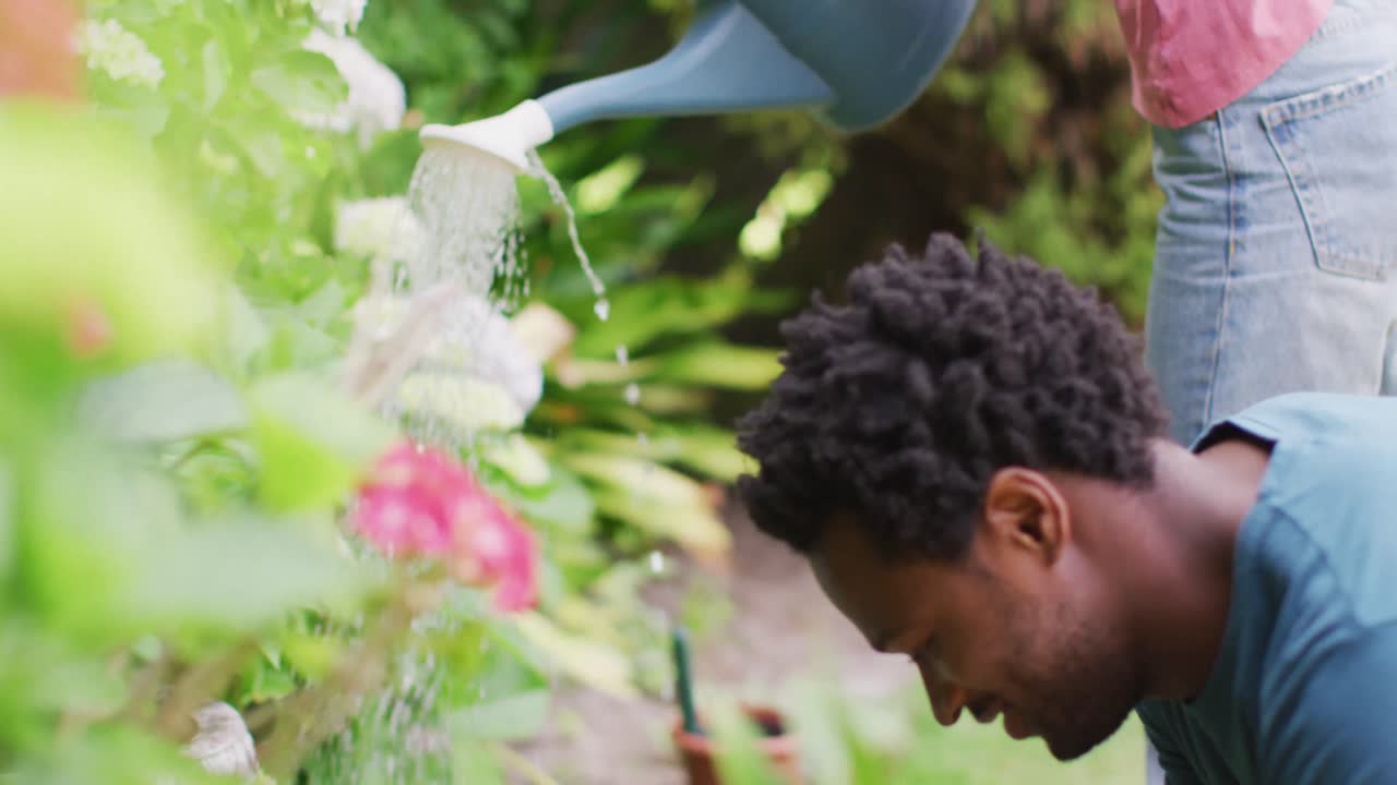 Happy biracial couple gardening together, planting flowers and watering plants