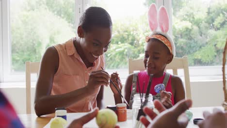 african american mother and daughter painting easter eggs together at home