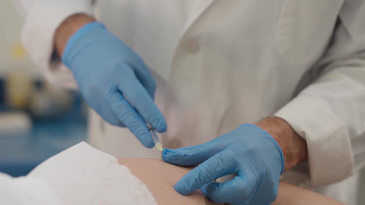 Close-up de mãos enluvadas trabalhando com uma agulha fina na pele de um paciente em uma clínica.