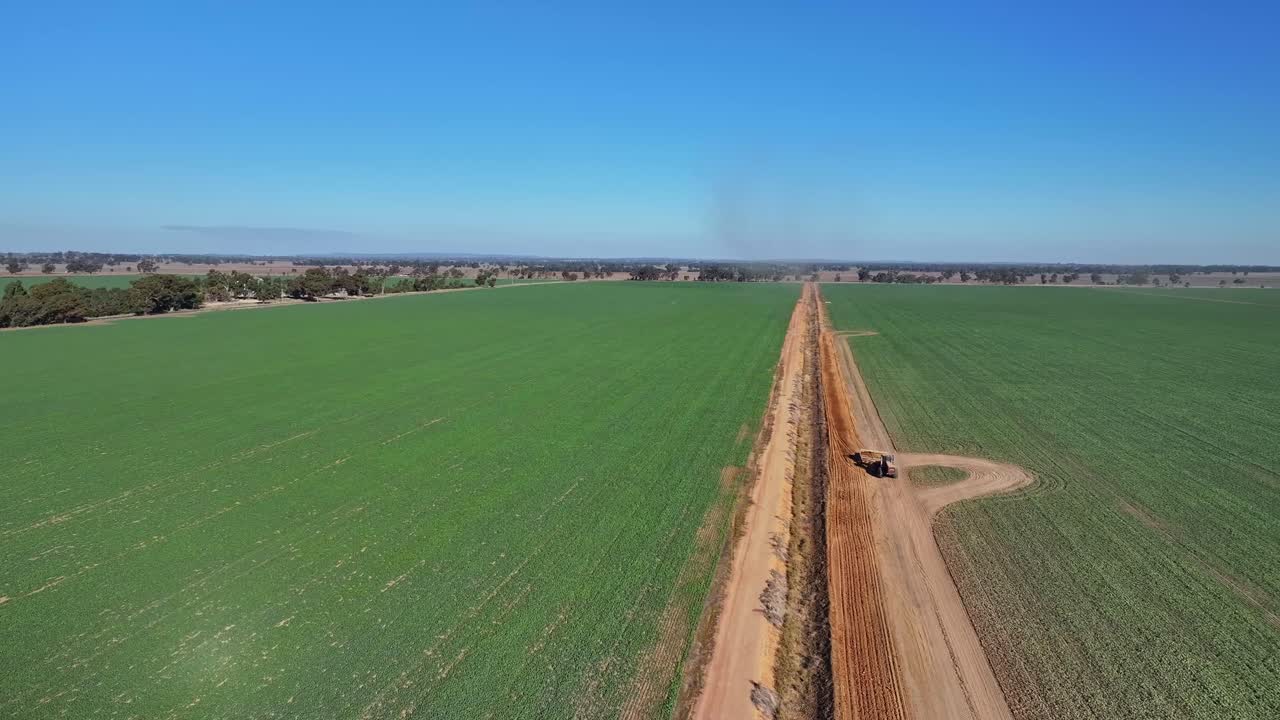 A tractor dragging a small road grader and scooping soil from a dirt road
