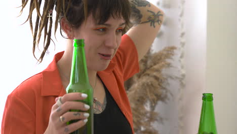 close up of a young woman with dreadlocks and tattoos drinking beer and talking with her friends during a party at home