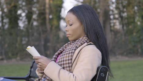 beautiful black young woman in park sitting on bench reading book trees cloudy day central london