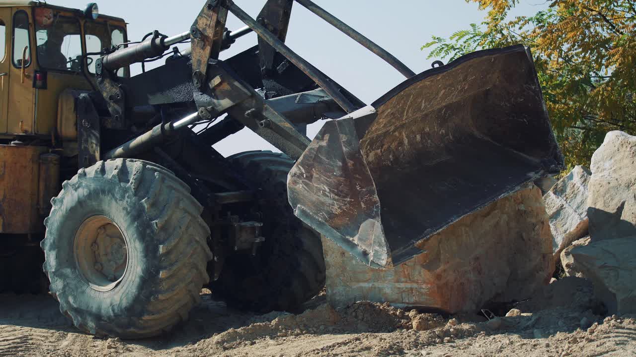 An old bulldozer at a quarry transports a large stone block. Excavator work in the mining industry