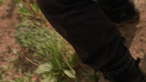 leg view of tourist boot stepping through overgrown slope, pressing down wild grass and sliding slightly while navigating unstable terrain near riverbank on sunny day in natural setting