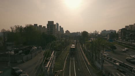 Vive-La-Cautivadora-Escena-De-Un-Tren-Que-Pasa-Velozmente-Al-Amanecer,-Filmada-En-Una-Estación-Adyacente-A-Una-Autopista,-Donde-La-Madrugada