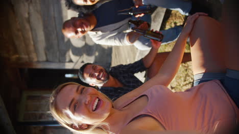video pov vertical de amigos de vacaciones sentados en el porche de una cabaña de campo bebiendo cerveza y tomando selfies