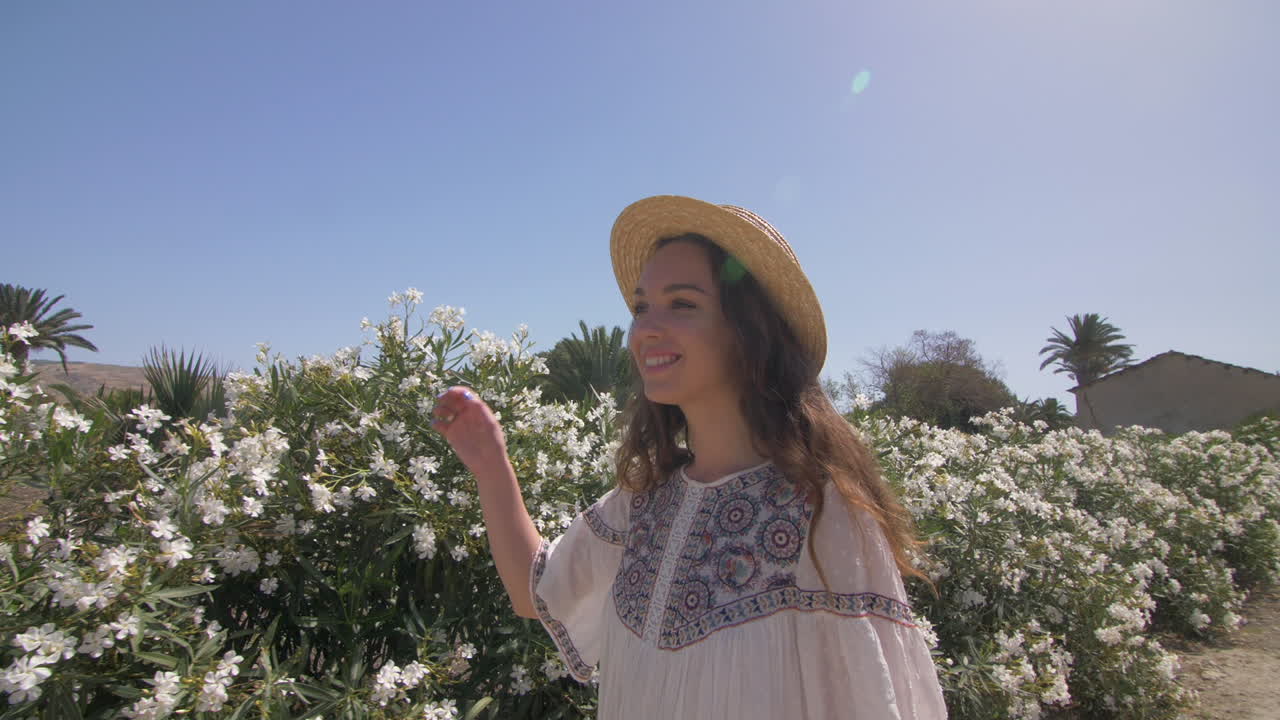 mujer sonriente en un vestido blanco y sombrero de pie en un campo de flores