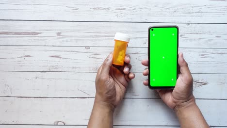 manos sosteniendo un frasco de pastillas y un teléfono con una pantalla verde