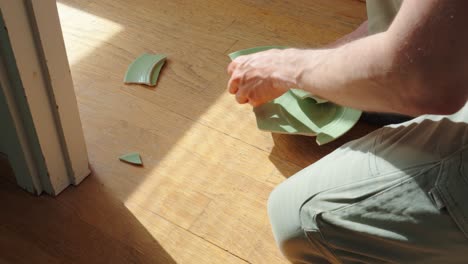 Man-picking-up-the-pieces-of-broken-plate-from-a-wooden-floor