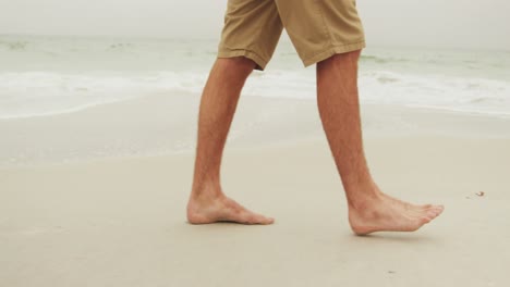 Low-section-of-man-walking-barefoot-on-the-beach-4k