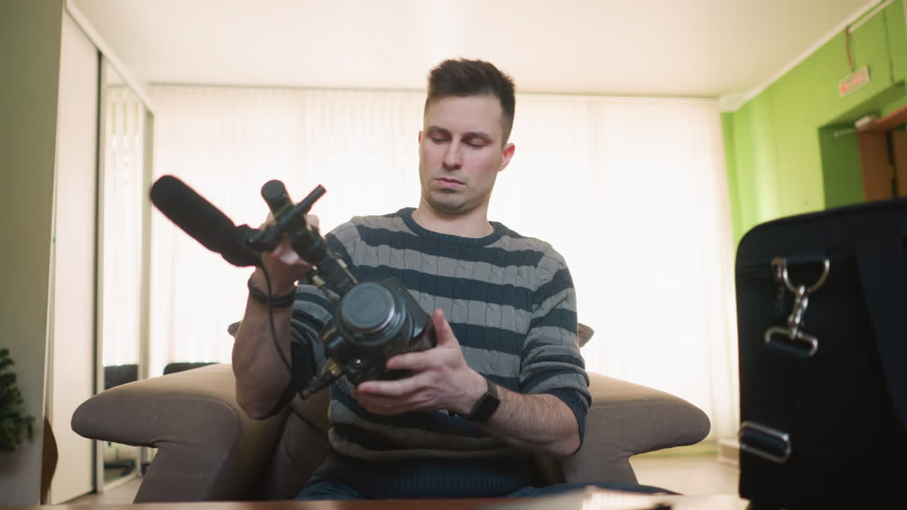 Homem pegando bolsa de equipamento de câmera na mesa, espaço de trabalho casual com equipamento de câmera como lente, fones de ouvido e smartphone. Paredes verdes brilhantes e móveis de madeira criando um ambiente confortável.