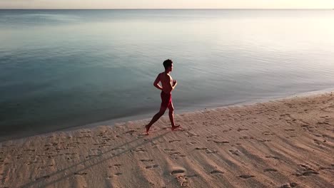 Toma-Aérea-De-Seguimiento-De-Un-Hombre-Trotando-En-Una-Hermosa-Playa-Tropical