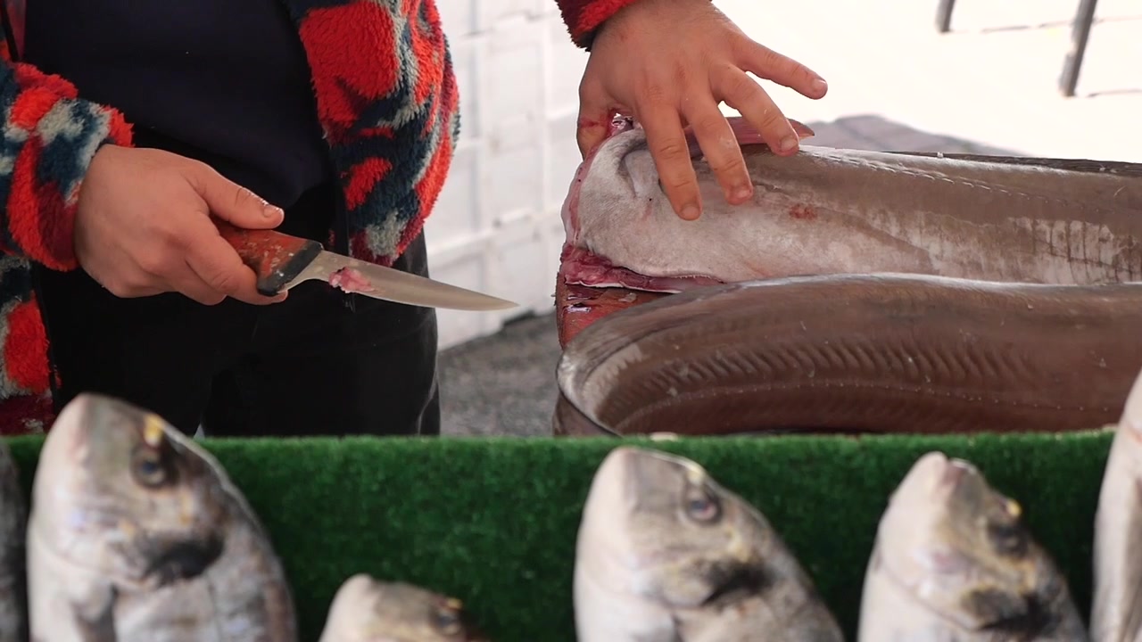 Fishmonger Cleaning and Preparing Fresh Fish at Market Stall