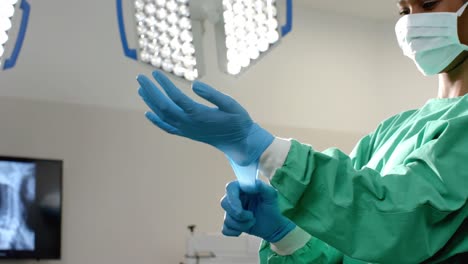 african american female surgeon wearing medical gloves in operating theatre, slow motion