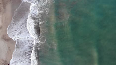 Aerial-4k-vertical-shot-by-a-drone,-of-the-blue-shorebrake-of-a-beach-in-the-Atlantic-Ocean,-Argentina