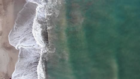 aerial 4k vertical shot by a drone, of the blue shorebrake of a beach in the atlantic ocean, argentina