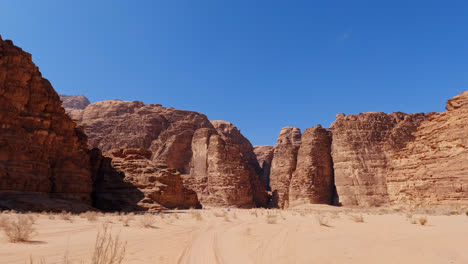 white sand below river valley of wadi rum, epic cliffs rise against blue sky