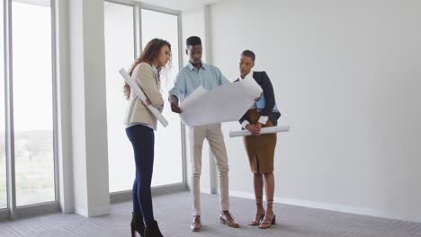 biracial female and male architects talking and checking architects plans in modern interiors