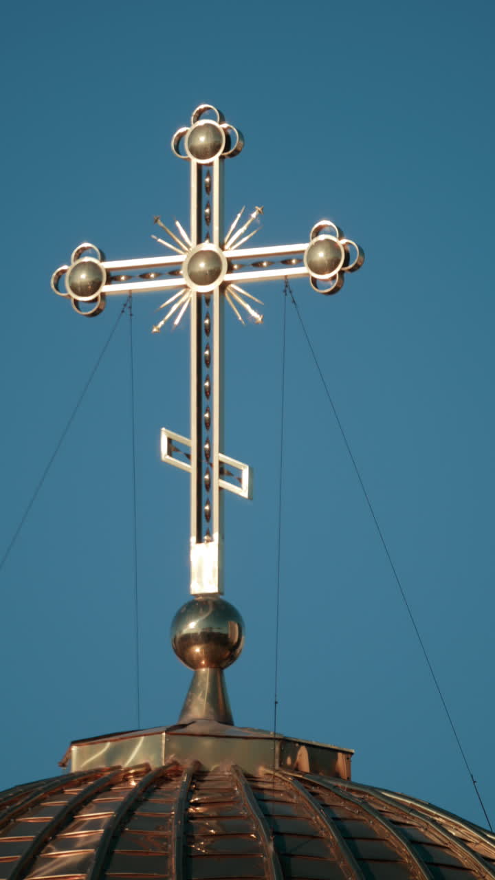Elegant metallic church cross glowing under clear blue sky. Vertical