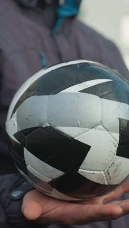 hombre hábilmente girando una pelota de fútbol en la palma de la mano con expresión enfocada, fondo borroso con edificios urbanos de gran altura y barra de malla