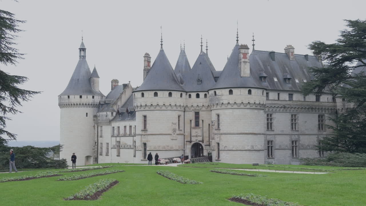 Tourists by Château de Chaumont and green lawn on cloudy day in France