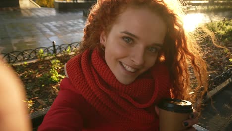 happy woman with long curly hair in a warm coat and scarf walks through the autumn park with yellow leaves