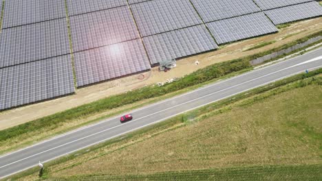 aerial isolated electric red car driving along asphalted road with solar panel photovoltaic power plant during a sunny day, rechargeable lithium battery zero emission alternative sustainable energy