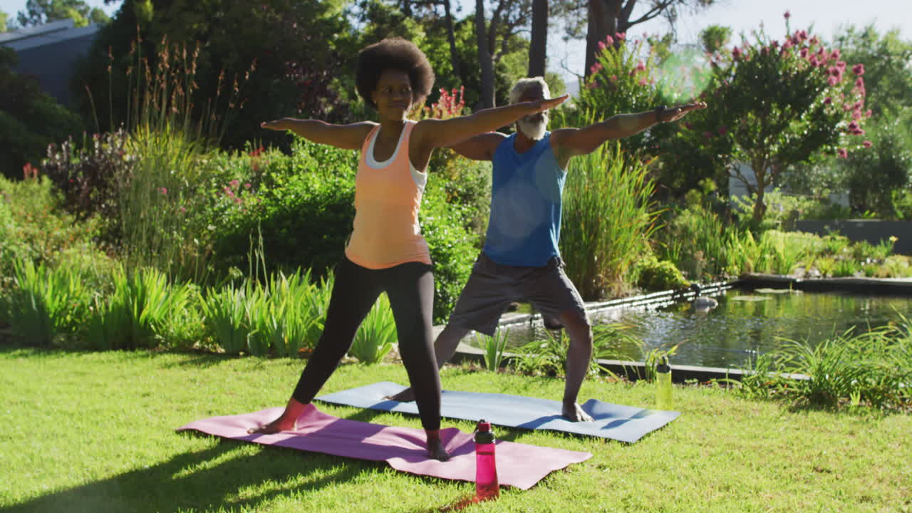 una pareja de ancianos afroamericanos haciendo ejercicio practicando yoga de pie en un jardín soleado